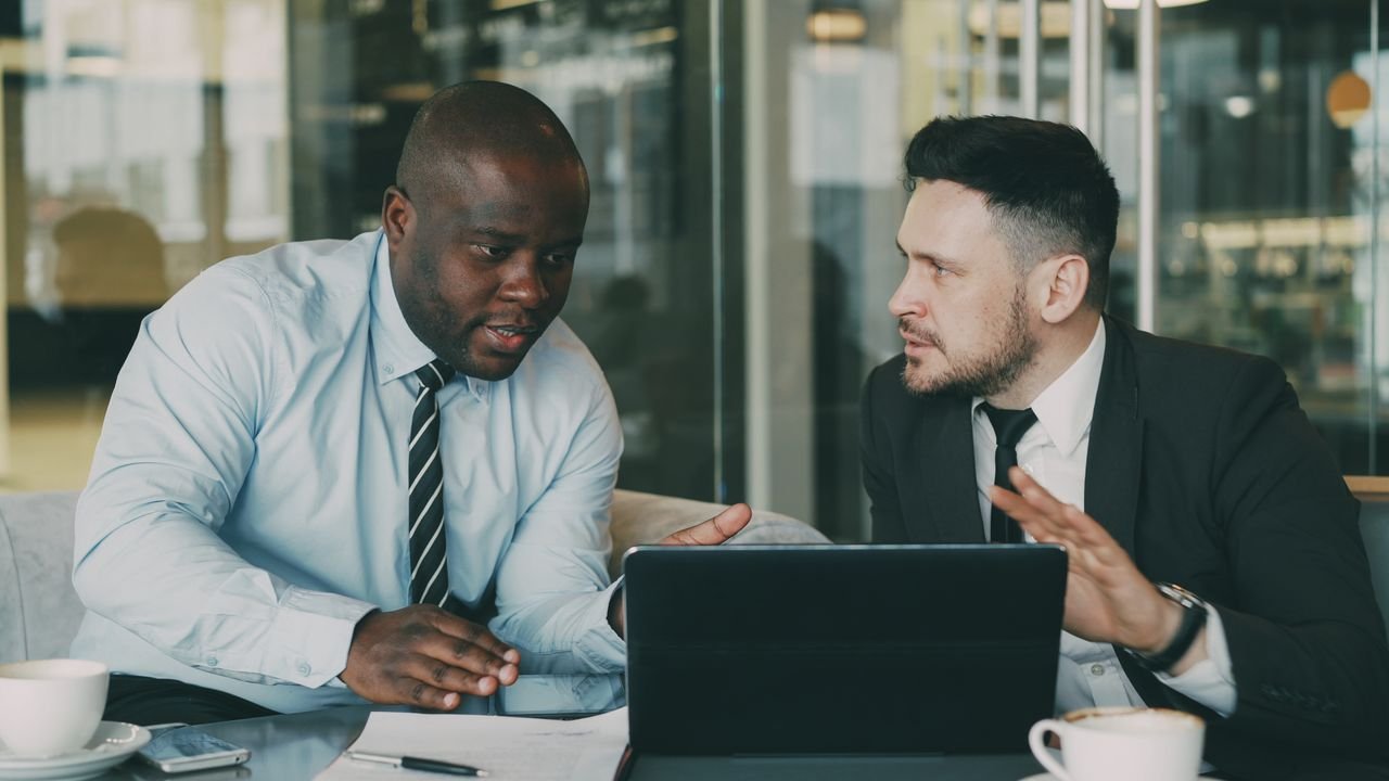 Two professionals discussing business strategies with a laptop in an office environment.